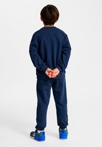 Mörkblå sweatshirt och mjukisbyxor i set, med avslappnad passform, ribbad mudd och matchande blåa träningsskor med grå detaljer.