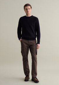 Marineblauer Strickpullover mit Rundhalsausschnitt, kombiniert mit braunen Cargo-Hosen mit Seitentaschen und dunkelbraunen Schnürschuhen.