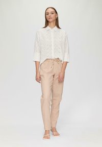 White shirt with eyelet patterns, collared, three-quarter sleeves, paired with light beige drawstring trousers and strappy sandals.