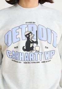 Felpa grigia con un orso a fumetti che tiene una pala, con testo blu che recita "DETROIT" e "CARHARTT WIP" sotto.