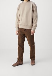 Beige sweatshirt med rund hals och ribbade ärmslut, parat med bruna denimbyxor. Skorna är bruna i mocka med texturerade detaljer.