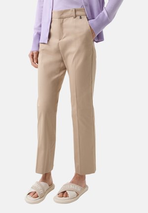 Beige op maat gemaakte broek met een gladde textuur, voorzien van een rechte voorzijde en zijzakken, gecombineerd met lichtbeige sandalen met logoaccenten.