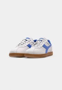 Bijele sneakers od antilopa s plavim detaljima, sa gumiranim potplatom i standardnim vezivanjem. Dizajn je zaobljen s glatkom teksturom.