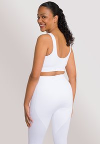 Top corto atletico bianco a righe e leggings a vita alta abbinati, con una texture liscia e un branding minimale sulla fascia in vita.