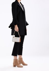 Černý kabát s volánkovými rukávy, bílý top, černé zkrácené džíny a béžové semišové kotníkové boty. Doplněno malou vzorovanou kabelkou.