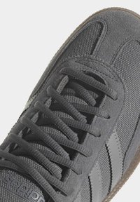 Gray sneaker with a textured suede upper, lace-up design, two gray stripes on the side, and a brown rubber sole.