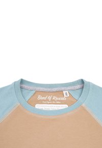 Lysbrun kortærmet t-shirt med aqua blå hals- og skulderdetaljer, der har en blød tekstur og et mærke for økologisk stofcertificering.