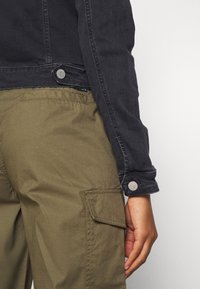 Black denim jacket with a fitted design and button accents, paired with olive green cargo pants featuring side pockets and a textured finish.