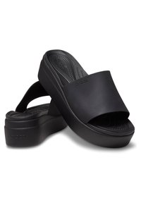 Sandales compensées noires à enfiler avec semelles épaisses et larges brides, présentant un discret logo "crocs" sur les côtés et les semelles intérieures.