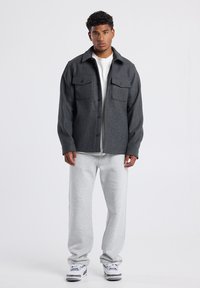 Gray textured jacket with two chest pockets, worn over a white t-shirt, paired with gray sweatpants and sneakers. Standing on a plain background.