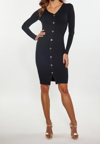 Robe noire à manches longues côtelée avec un col en V et des boutons dorés sur le devant ; longueur genoux avec une fente à l'ourlet.