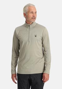 Lange mouwen pullover in lichtgrijs, gemaakt van vochtregulerende stof met een hoge ritssluiting en een klein zwart spinnend logo op de borst.