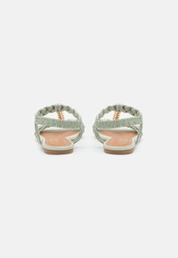 Grønne flettede sandaler med en flat tan såle og elastiske stropper. Har en glatt tekstur og subtile design detaljer.