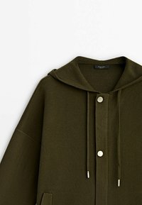 Sweat à capuche vert foncé avec fermeture à boutons à l'avant, cordons de serrage et un petit détail de poche sur le côté gauche avant.