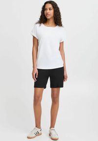 Hvit kortermet t-skjorte kombinert med svarte shorts. Antrekket har en avslappet passform, glatt tekstur og et uformelt design med minimal detaljering.