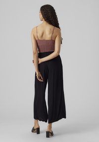 Mauve színű horgolt cropped top, laza fekete széles szárú nadrággal párosítva. A top vékony pántokkal és texturált részletekkel rendelkezik; a nadrág laza szabású.