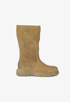 Bota alta de ante marrón con puntera redondeada y suela de goma texturizada. Presenta un diseño sencillo con costuras visibles y un pequeño detalle de etiqueta.