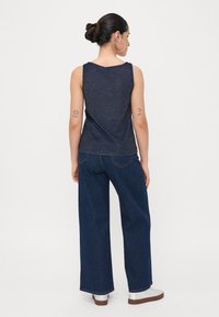 Un haut sans manches bleu foncé avec un léger éclat, associé à un jean en denim à taille haute et à jambes larges. Des chaussures à plateforme argentées complètent la tenue.