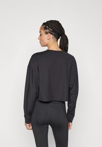 Schwarzes, kurz geschnittenes Langarmoberteil mit lockerer Passform, aus weichem Material, kombiniert mit hochgeschnittenen schwarzen Leggings. Minimalistisches Design, ohne Muster.
