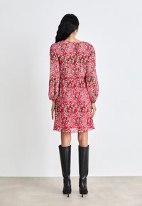 Robe fleurie rose avec de longues manches bouffantes, en matière transparente, taille froncée et ourlet fluide, associée à des bottes noires montantes.
