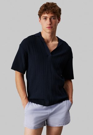 Navy short-sleeve pullover with a textured knit pattern and a wide collar. Paired with light gray shorts featuring side pockets.