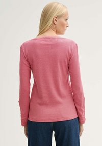 Chemise à manches longues en rose pâle avec un subtil motif de rayures horizontales. Présente un col bateau et des manches ajustées, fabriquée dans un tissu doux.