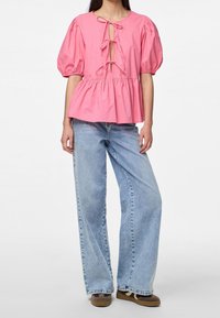 Top de algodón rosa con mangas abullonadas y cierre de lazo en el escote; combinado con jeans de mezclilla de pierna ancha en azul claro.