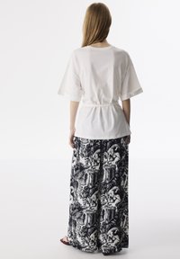 Witte katoenen t-shirt met korte mouwen en een cinched taille, gecombineerd met zwart-witte breed legging met ingewikkelde patronen.