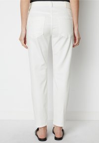 Vita denimbyxor med rak skärning, med fickor på baksidan. Slät textur och enkel design. Bärs med svarta sandaler.