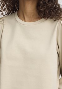 Beige sweatshirt i mjukt tyg, med rund halsringning och mjuka puffärmar, med en slät yta och minimalistisk design.