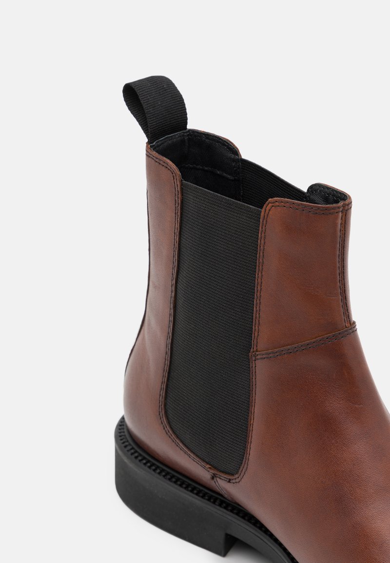 Brun läderankelboot med elastiska sidopaneler, svart textilfoder, robust sula och en dragflik baktill för enkel påtagning.