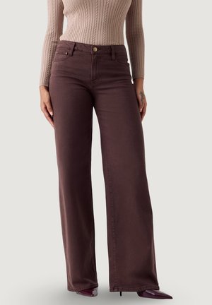 Donna che indossa jeans marroni a vita alta con gamba larga abbinati a una maglia a coste beige a maniche lunghe e stivali con punta appuntita.