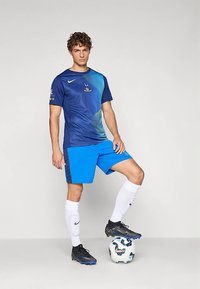 Blå Nike-drakt med gradientdesign, blå shorts, hvite sokker og svarte fotballsko. Står på en mønstret fotball.
