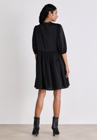 Rochie neagră cu sleeve pufoase, talie strânsă și fustă evazată. Material neted, până la genunchi, purtată cu botine negre cu toc.