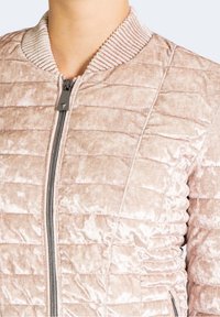 Pohodlná bombarďácká bunda z měkkého, světlého růžového sametu. Disponuje žebrovaným límcem a zipovým zapínáním, s horizontálním prošíváním.