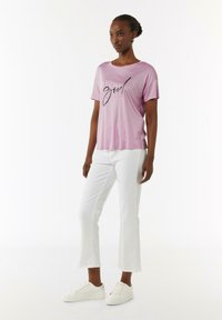 Pink cotton t-shirt with short sleeves and a round neckline, featuring a black graphic text print, paired with white cropped pants and white sneakers.