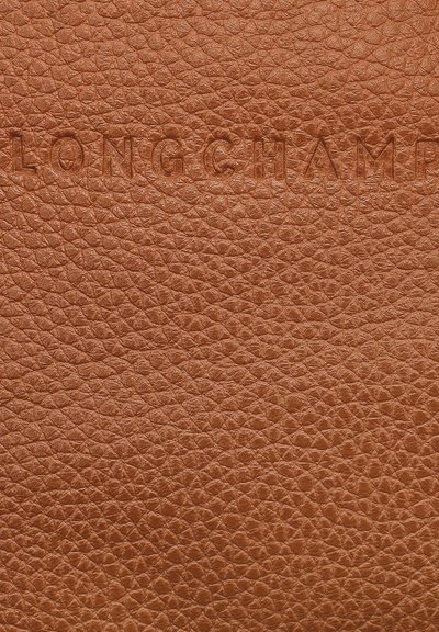Braunes, strukturiertes Leder mit eingeprägtem "LONGCHAMP"-Logo. Die Oberfläche weist ein genoppte Muster auf, das Tiefe und visuelles Interesse verleiht.