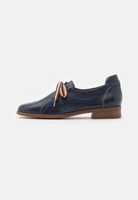 Chaussure en cuir bleu marine avec un bout arrondi, des coutures minimales et un petit talon marron. Dispose d'un lacet fin dans des tons clairs et foncés.