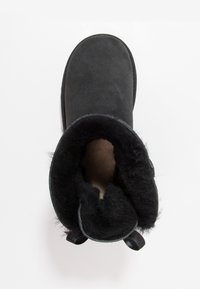 Svart mockaboot med mjukt fluffigt foder och rundad tå. Har dubbla svarta tygöglor vid hälen för enkel av-och-påtagning.