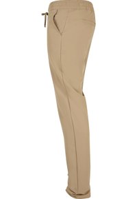 Pantalon beige décontracté avec taille élastique, poches latérales et cordon de serrage, vu de profil.