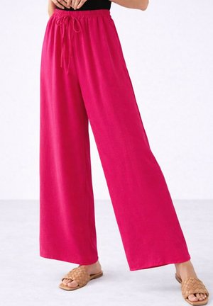 Pantalon large rose vif avec taille élastique et cordon, porté avec des sandales tressées beiges à enfiler.