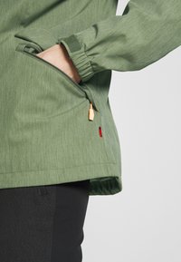 Green jacket features a textured, heathered fabric. Includes a zippered pocket with wooden accents and a Velcro adjustable cuff.