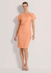 Kurzärmliges, knielanges Kleid aus weichem Pfirsichstoff mit einem gerafften Halsdetail. Glatte Textur und taillierte Silhouette.