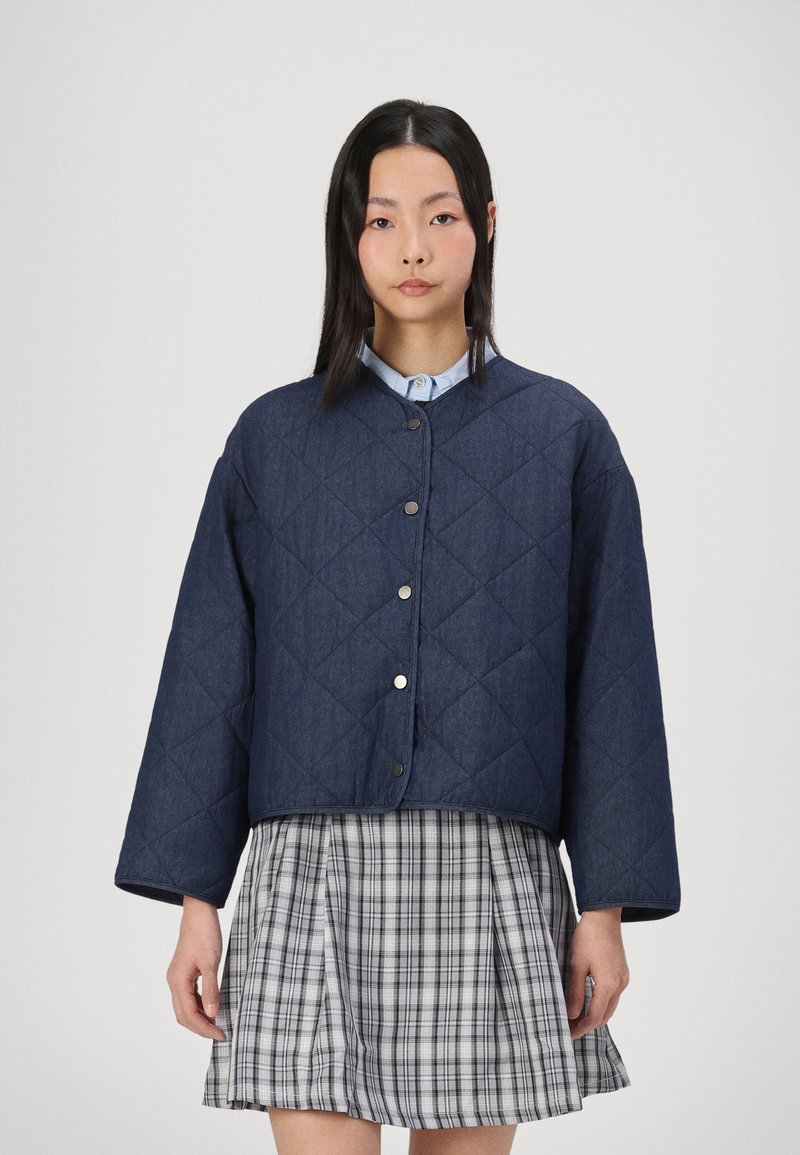 Donker denim gewatteerde jas met een ronde kraag, drukknoopsluitingen en oversized mouwen, gecombineerd met een geruite rok.