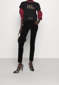 Camiseta negra con logo "RL" de lentejuelas, superpuesta sobre una camisa a cuadros en rojo y negro. Combinada con pantalones de pana negros y tacones de estampa.