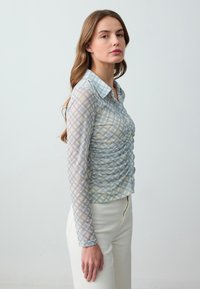 Camicia a maniche lunghe con bottoni, in un motivo a quadri blu chiaro e crema, caratterizzata da una texture arricciata sulla parte anteriore, tessuto trasparente e colletto classico.