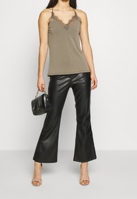 Olivgrön linne med spetsdetaljer, kombinerat med svarta fusk läderbyxor med svängd ben. Accessoarer inkluderar en liten svart handväska och nude sandaler.