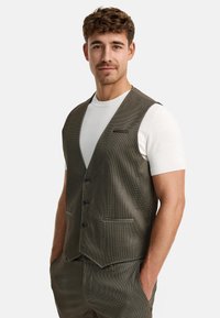 Braun karierter Weste mit V-Ausschnitt, Knopfverschluss und zwei Fronttaschen. Über einem weißen kurzärmeligen Hemd getragen, das eine glatte Textur zeigt.