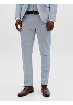 Mand iført lysegrå habitbukser, brunt læderbælte og polerede brune festlige sko, der står mod en hvid baggrund.