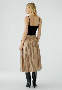 Zwarte mouwloze top, gouden metallic midi rok met een glanzende, geplooide textuur en elastische tailleband; zwarte knie-high laarzen.